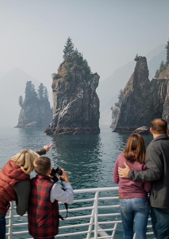 People stand at the guard rail of a tour boat looking out at rocky cliffs in the sea.