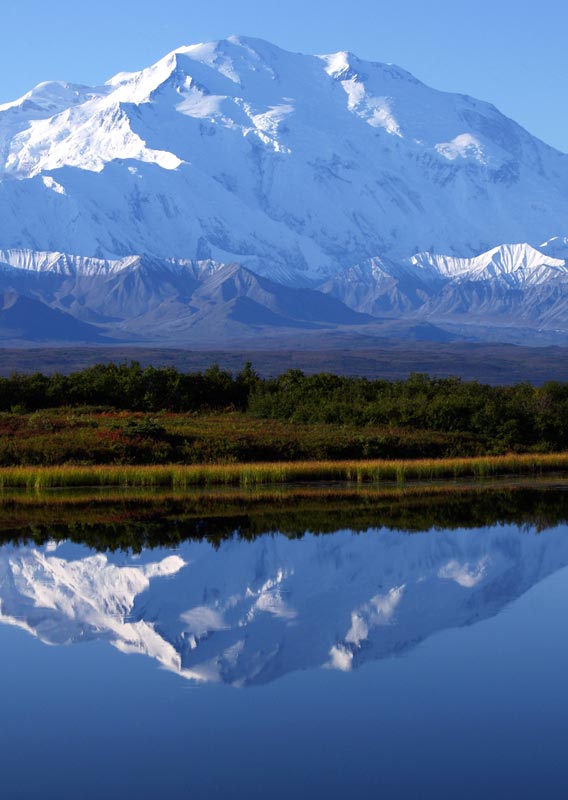 A massive snow-covered mountain rises above tundra