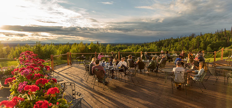 People sitting at dining tables on a patio at sunset