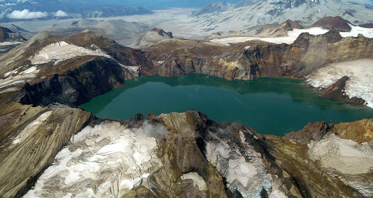 A turquoise blue lake nestled around mountains and snow.