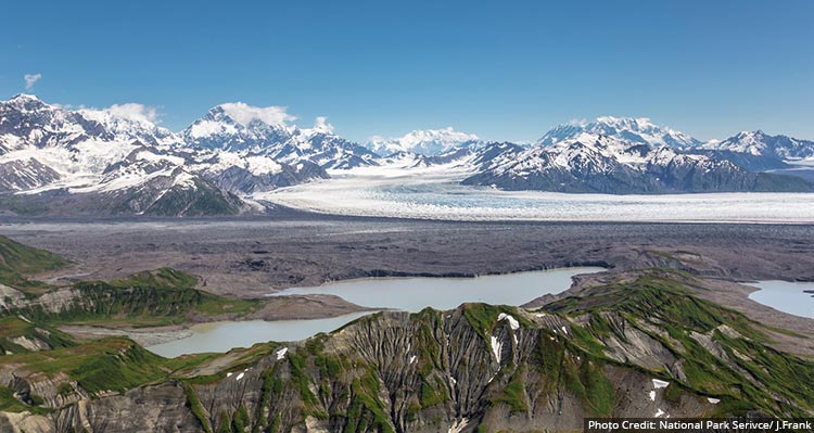 A landscape with snow covered mountains, lakes and small green topped mountains.