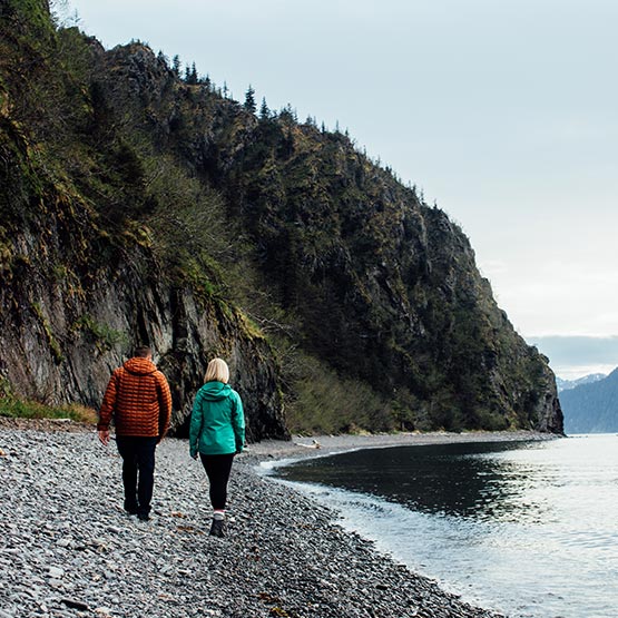 Two people walk along a rocky beach.