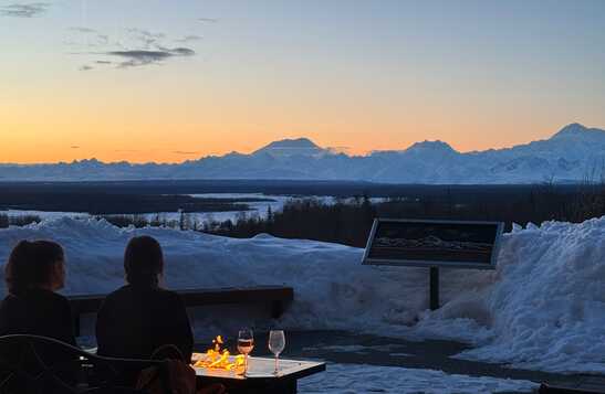 Two people sitting by a fire pit looking at the mountains