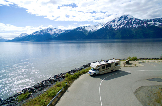 RV travelling down a road past water and mountains