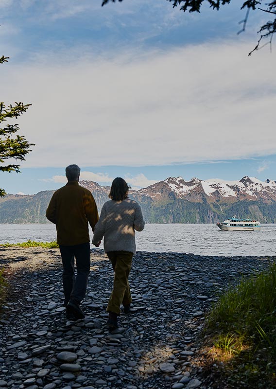 Two people walk on a rocky pathway to a seashore.