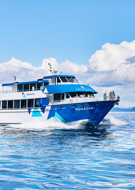 A Kenai Fjords Tours boat sailing past mountains and an island.