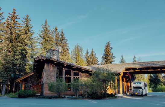 A wooden hotel building below tall conifer trees.